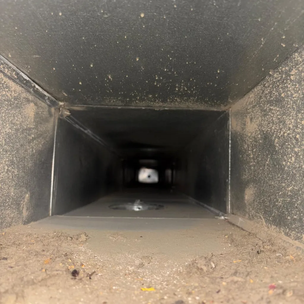 Inside a rectangular supply duct with dust and debris along the bottom, before cleaning