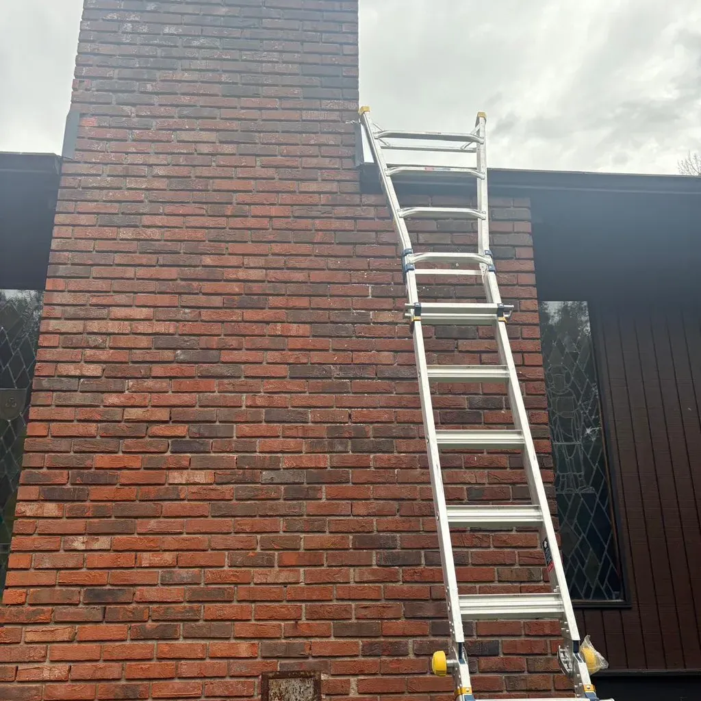 Ladder set against a tall brick chimney for work from the roof