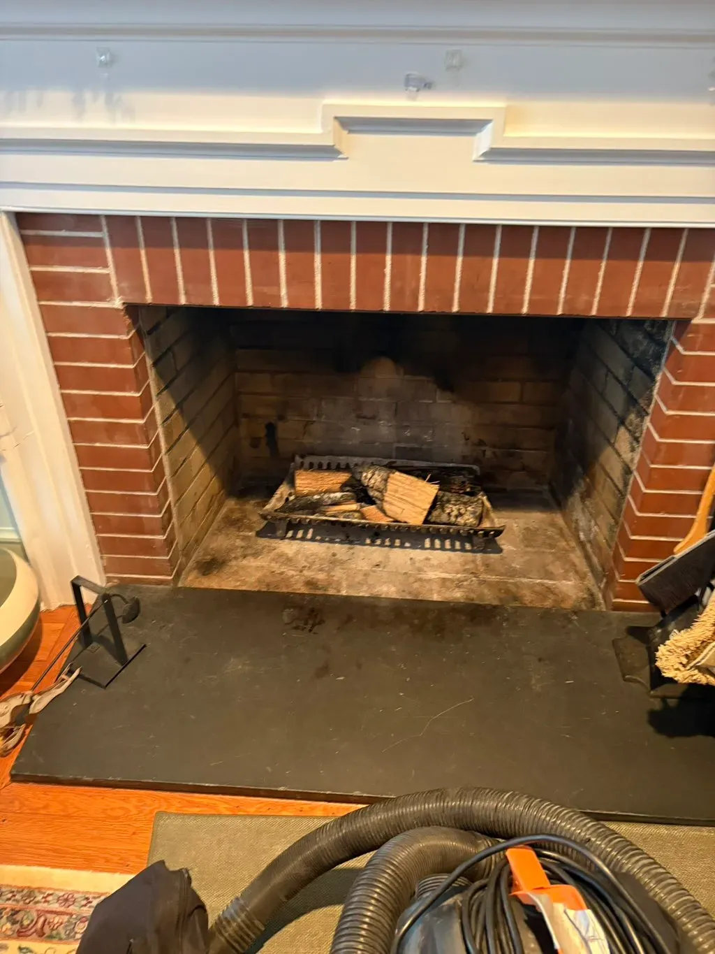 Chimney sweep in progress, the vacuum hose in the firebox of a brick fireplace