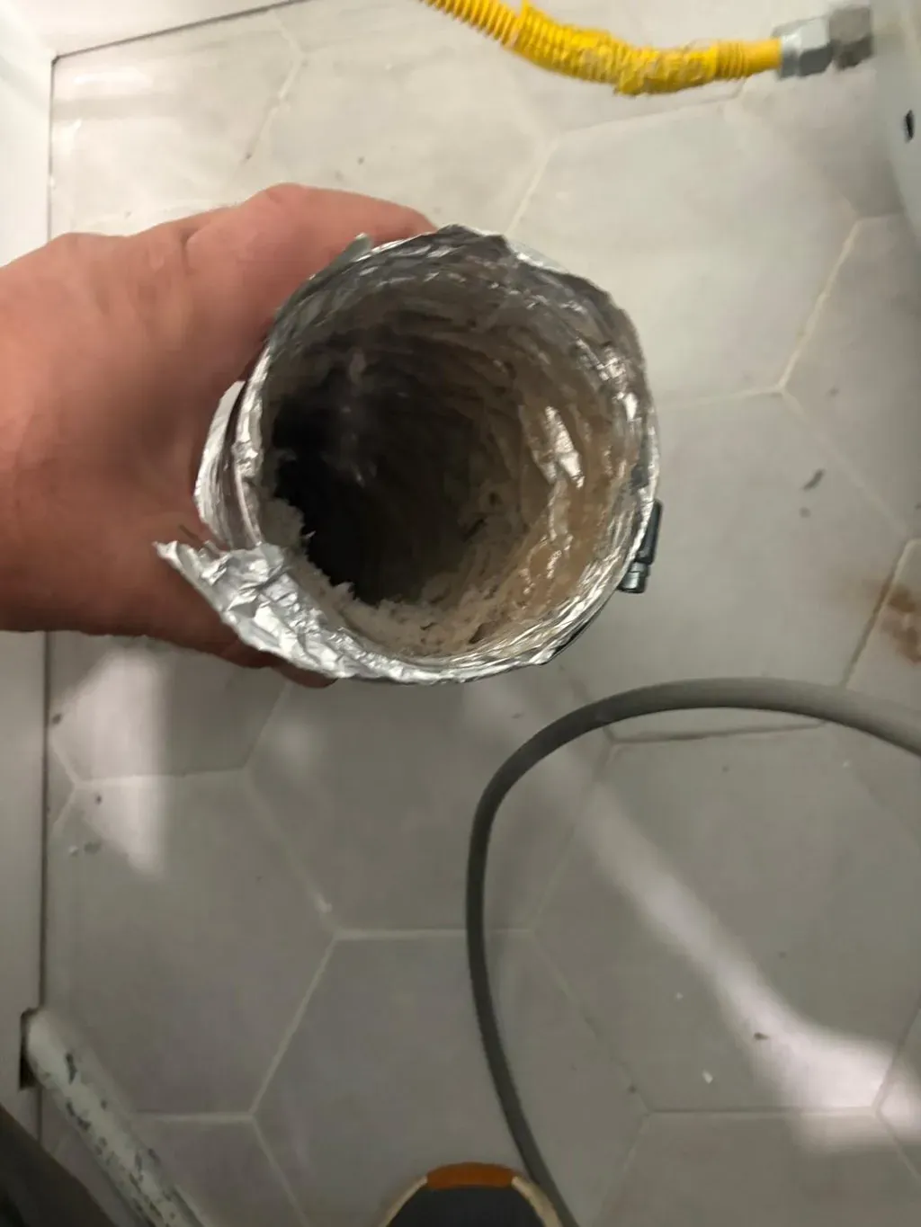 A crushed lint-filled dryer duct held in the hand after removal