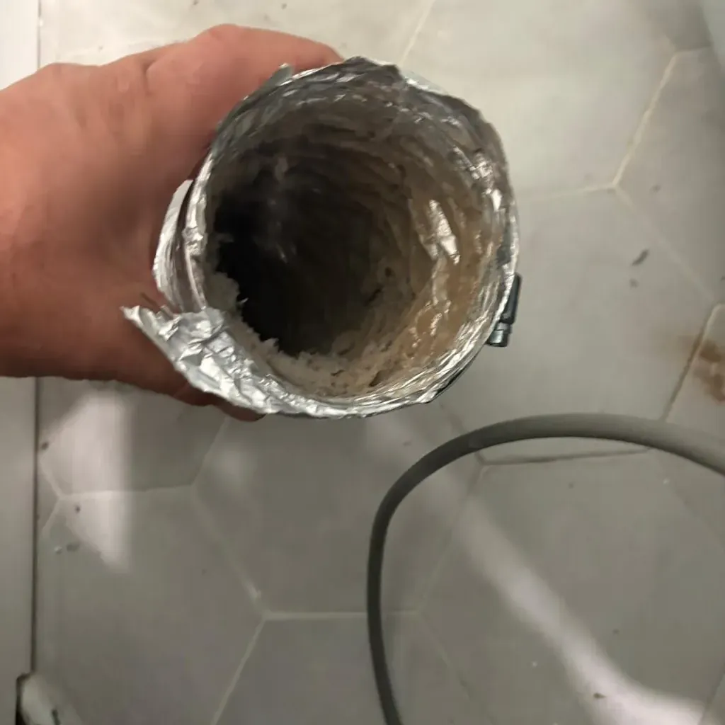A crushed lint-filled dryer duct held in the hand after removal