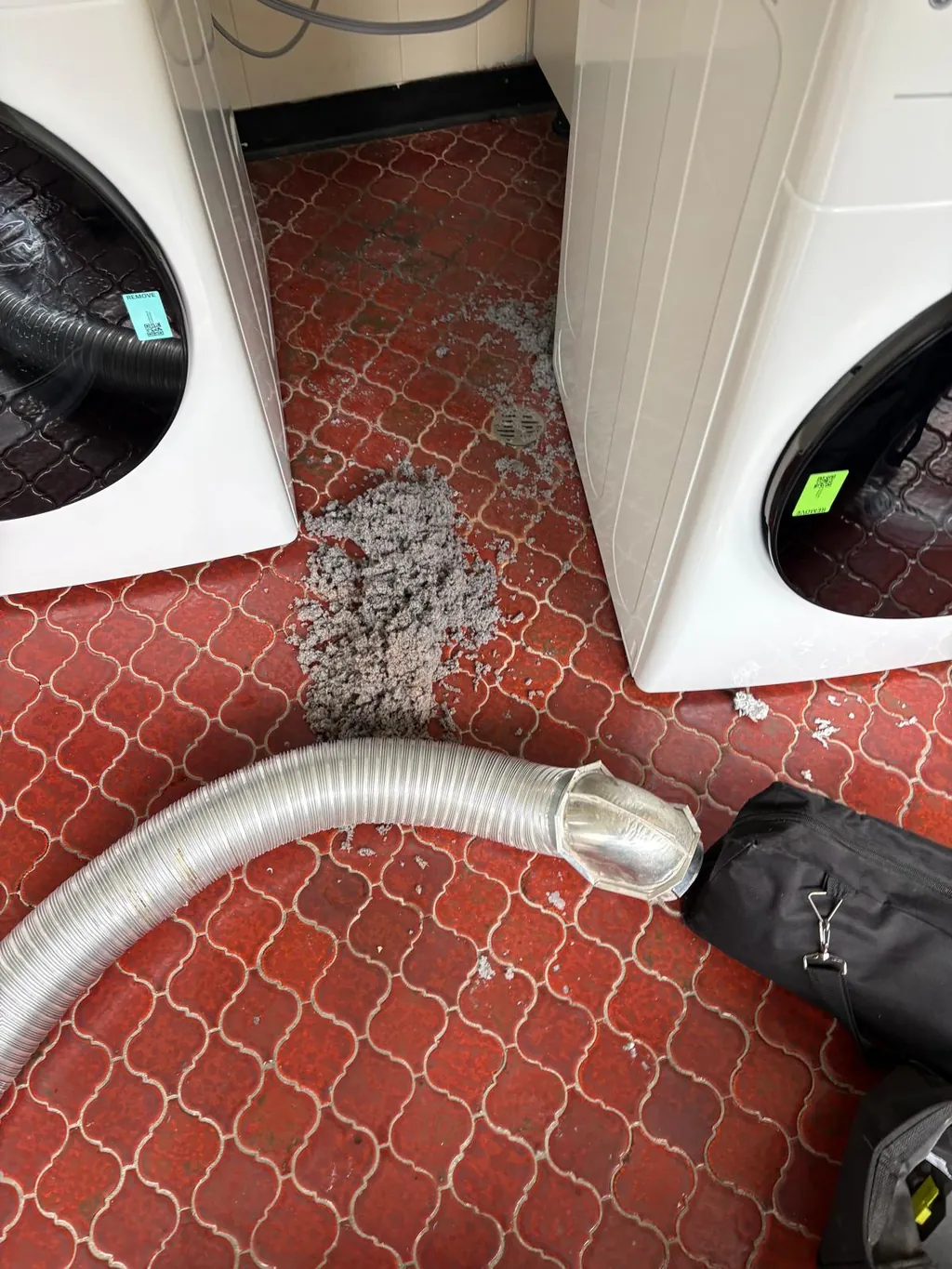 Dryer vent cleaning in a laundry room: lint on the floor beside the dryer and the vacuum hose