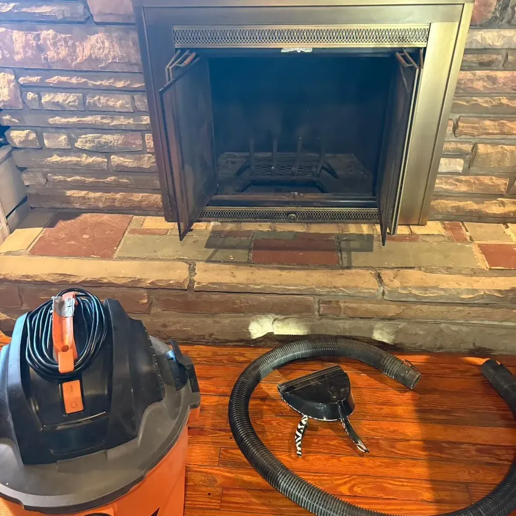 Vacuum, hose and brush laid out at a glass-door fireplace insert